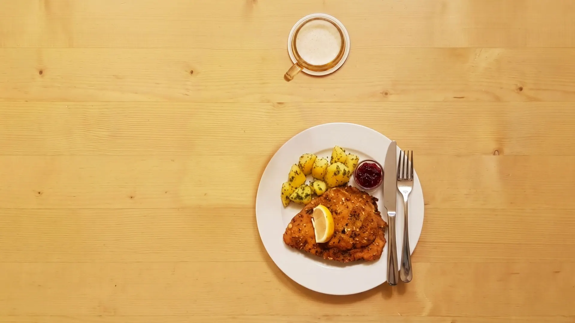 Draufsicht auf einen Teller mit Wiener Schnitzel, Petersilerdäpfeln und Preiselbeeren neben dem Bierglas.